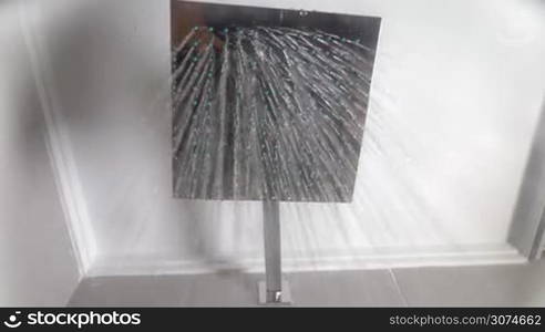 Slow motion bottom shot of working big modern shower with square showerhead, water streams falling to the camera