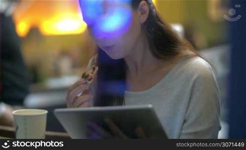 Slow motion clip of a brunette woman eating cake with jam and reading on electronic tablet in the restaurant
