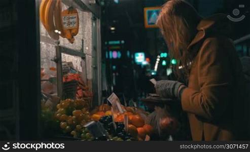 Slow motion clip of a young woman in the coat buying products in the stall outside in the evening on rainy day