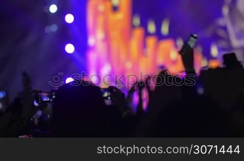 Slow motion clip of the people having a good time on the pop concert, they take photos and put their hands up during the concert, the stage with candles in red