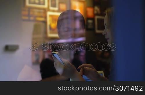 Slow motion clip of view through restaurant glass of woman and man discussing some topic, woman shows something on the smartphone and gesticulates
