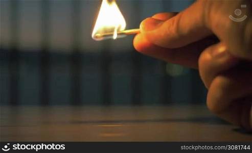 Slow motion close-up shot of a match stick burning in hands. Bright flame flickering out in the darkness