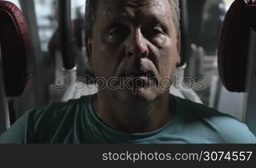 Slow motion close-up shot of a senior man being tired and sweaty. He looking to the camera with exhaustion after hard workout