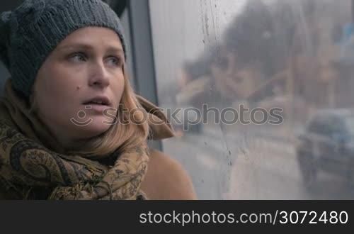 Slow motion close-up shot of a young sad woman traveling by bus on a dull rainy day. She looking out the wet window and breathing heavily. Loneliness in a big city