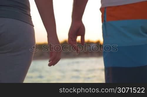 Slow motion close-up shot of man and woman walking by the sea and holding hands. Love and devotion