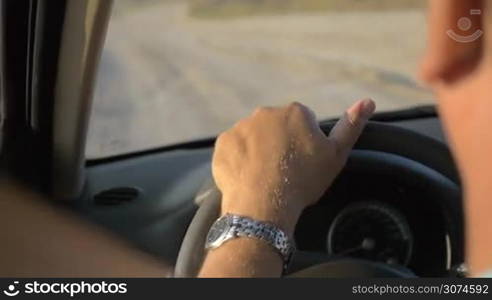 Slow motion close-up shot of man driving a car in the countryside in summer evening. View to the road and hands on the steering wheel