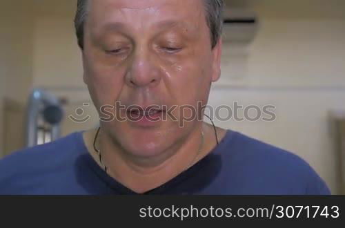Slow motion close-up shot of man getting exhausted during workout on treadmill. He wiping sweat with hand and breathing deeply