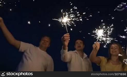 Slow motion dolly shot of happy and excited family of four having fun with sparkles outdoor at night