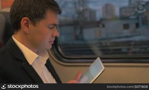 Slow motion of a businessman traveling by train and working with touch pad. Message typing or internet browsing