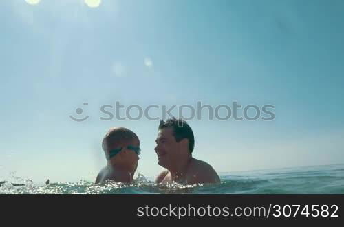 Slow motion of a family bathing in the sea. Father taking son and throwing him up against the bright sunshine, mother splashing water. Happy summer vacation