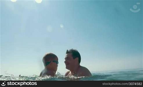 Slow motion of a family bathing in the sea. Father taking son and throwing him up against the bright sunshine, mother splashing water. Happy summer vacation