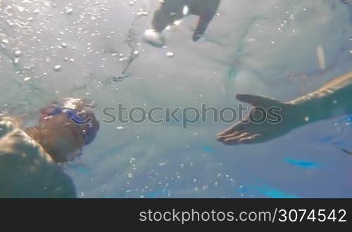 Slow motion of a father swimming to the son and taking him in arms. Underwater shot in swimming pool on sunny day