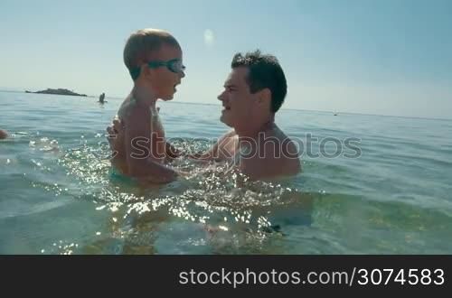 Slow motion of a father throwing son up from the sea. High fly from the water in dads hands against bright shining sun. Happy summer holidays