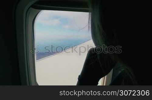 Slow motion of a female passenger enjoying outside view flying in the plane. Land and airplane wing can be seen through the window