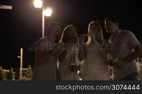 Slow motion of a four happy friends taking selfie with smart phone in the street while they having night outing and drinking coffee