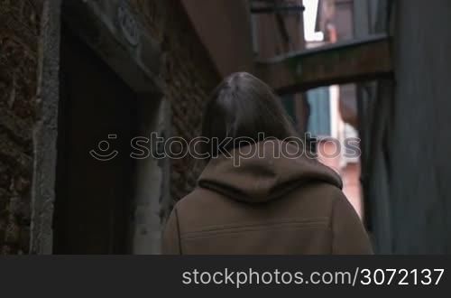 Slow motion of a happy young woman wandering among worn grungy buildings of old city and looking around
