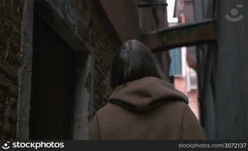 Slow motion of a happy young woman wandering among worn grungy buildings of old city and looking around