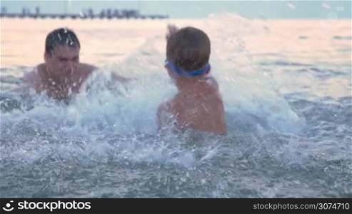 Slow motion of a little boy in goggles having sea battle with father. They having fun while splashing water strongly