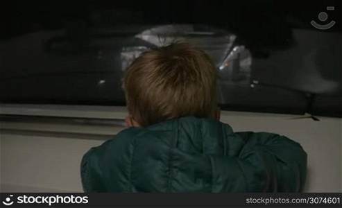 Slow motion of a little boy in jacket looking through the window of underground train arriving to the station, back view