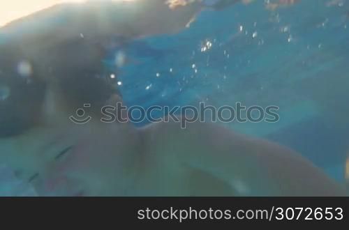 Slow motion of a little brave child swimming underwater in the pool. Sunlight coming through the clear water. Physical activity and recreation