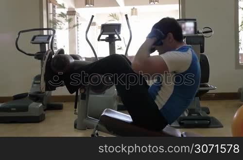 Slow motion of a man exercising on modern equipped fitness center. He doing sit-ups on abdominal bench and then stopping for a break