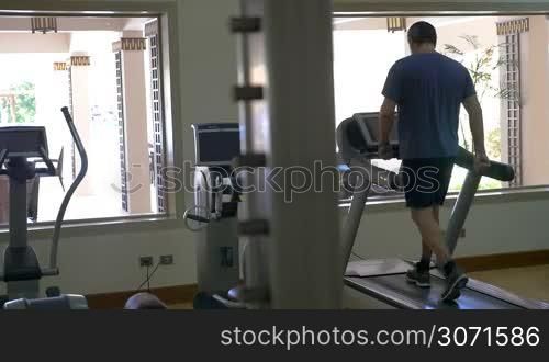 Slow motion of a man training on treadmill in light and modern eqipped gymnasium. Cardio machine keeping him fit