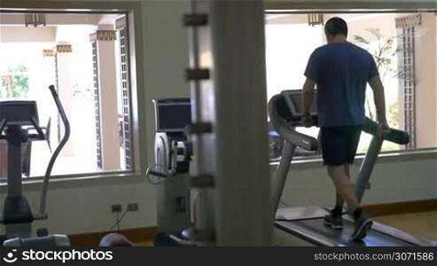 Slow motion of a man training on treadmill in light and modern eqipped gymnasium. Cardio machine keeping him fit