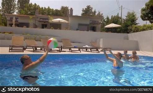 Slow motion of a mother and grandfather playing volleyball in the outdoor pool while boy and grandmother watching them. Happy summer time at vacation home