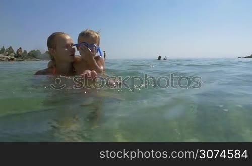 Slow motion of a mother and son bathing in sea. She holding little boy in arms and he splashing water with feet. Child having playful and happy look