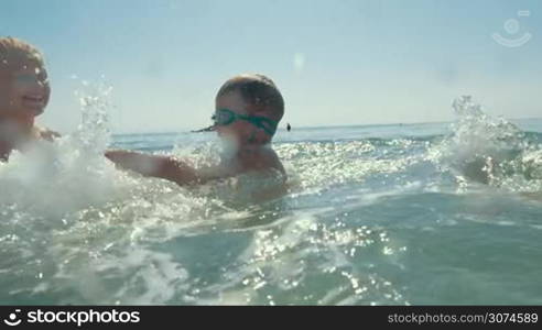 Slow motion of a mother, father and little son in goggles splashing water while bathing in the sea on hot summer day. Water sparkling in bright sunlight