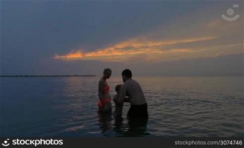 Slow motion of a parents and son bathing in the sea at twilight. Father holding son in arms. Family summer vacation
