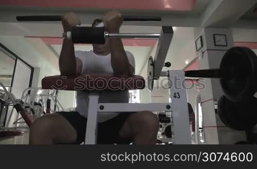 Slow motion of a senior man working out on fitness machine and training hand muscles. Regular visits to gym making him strong and healthy