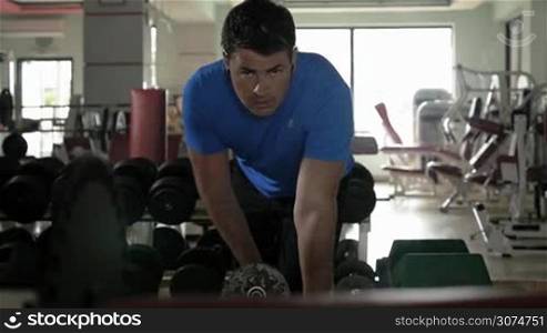 Slow motion of a strong sportive man doing working out with dumbbell in the gym, he listening to music in headphones while training