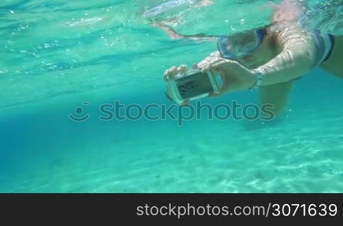 Slow motion of a woman in snorkel diving with smart phone in water-proof case. Making selfie or taking pictures underwater