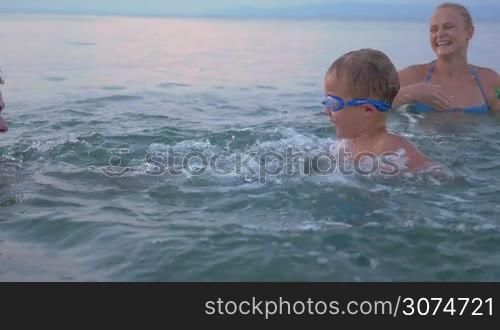 Slow motion of a young family with little child having enjoyable time in the sea. They splashing water to each other and laughing. happy vacation time