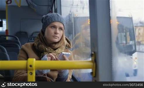 Slow motion of a young woman taking away cell phone and looking out the bus window. Routine ride in the city on a dull day