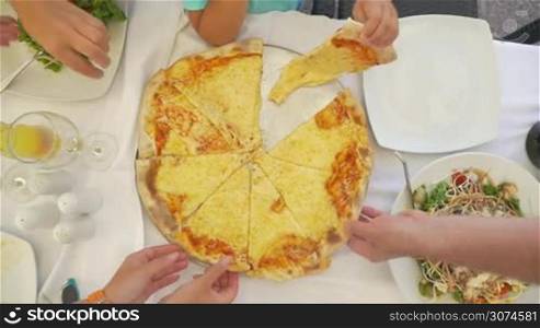 Slow motion of adult people and child taking cheese pizza from the tray during dinner in the restaurant or cafe. Top view with only hands to be seen