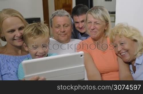 Slow motion of big family watching film on tablet computer at home. It making them smile and laugh