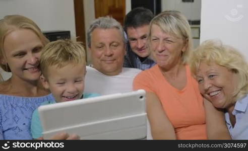 Slow motion of big family watching film on tablet computer at home. It making them smile and laugh