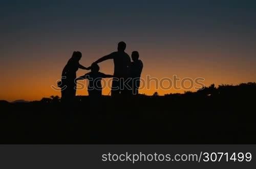 Slow motion of big family with child in a cicrle holding hands. Their black silhouettes against colorful evening sky