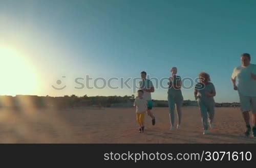 Slow motion of big family with little child jogging on the beach in bright evening sunlight. Sports activity on vacation