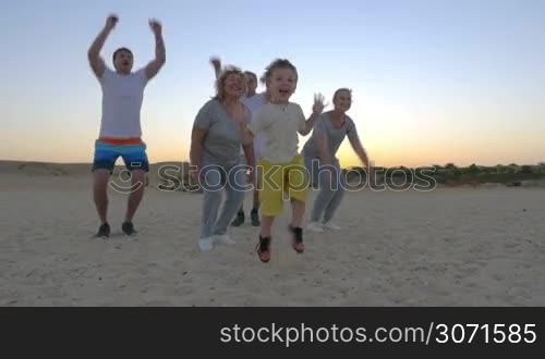 Slow motion of big family with parents, son and grandparents jumping on the beach being happy and excited