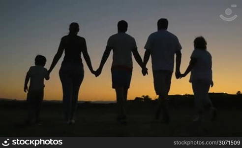 Slow motion of child, parents and grandparents walking on the beach. They holding hands and then putting them up on background of bright evening sky