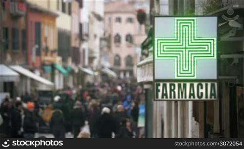 Slow motion of crowd walking in the street and pharmacy banner with led green cross in foreground