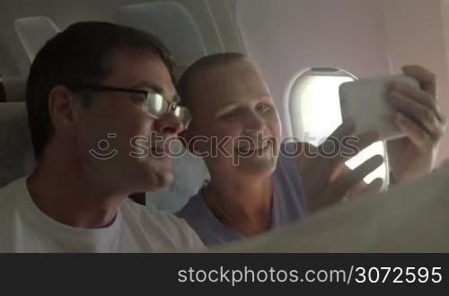 Slow motion of excited couple making selfie with cell phone in airplane. Taking a shot of happy traveling when they are together