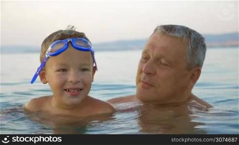 Slow motion of grandfather and grandson swimming in the sea. Man holding boy in arms and they both enjoying warm water