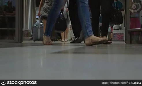 Slow motion of group of people with baggage walking out the airport terminal, only feet can be seen. Business trips and vacation