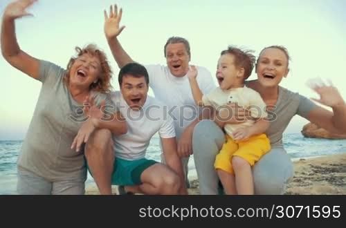 Slow motion of happy and excited family by the sea on the beach. Smiling grandparents, parents and little son waving hands. Enjoyable vacation time