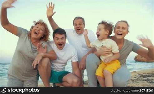 Slow motion of happy and excited family by the sea on the beach. Smiling grandparents, parents and little son waving hands. Enjoyable vacation time