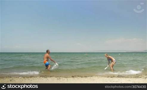 Slow motion of happy couple splashing water with paddles and playing tennis in water with ping pong rackets. Man falling into the sea after hitting the ball